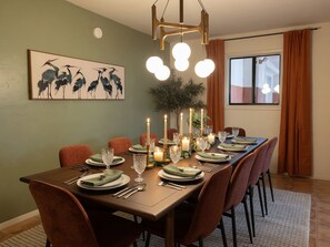 A dining room with a long table set for six, featuring a chandelier, candles, and a painting of birds on the wall. - Hot tub + Gameroom + Yard Firepit near White sands (Alamogordo)