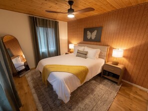 A hotel room with a bed, a ceiling fan, a wall-mounted butterfly art piece, and a nightstand with a lamp. - Hot tub + Gameroom + Yard Firepit near White sands (Alamogordo)