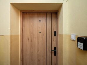 A wooden door with a number '2' on it, a black handle, and a wall-mounted device to the right. - Manufaktura Cosy Apartment (Łódź)