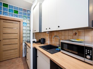 A modern kitchen with white cabinets, a black sink, a microwave, and a coffee maker. - Manufaktura Cosy Apartment (Łódź)