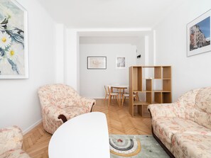 Ein Wohnzimmer mit floralen Sofas, einem Holzregal und einem Essbereich mit weißem Tisch und Stühlen.