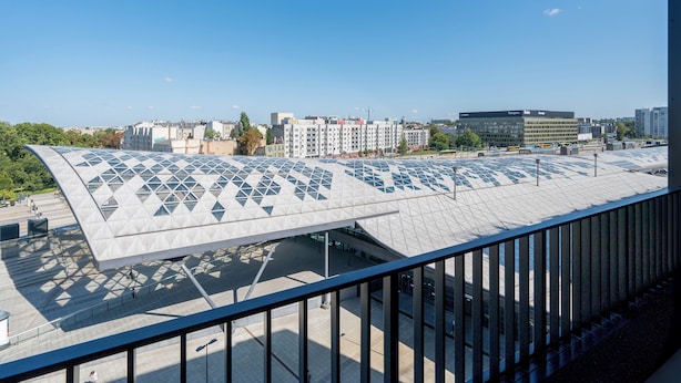 A modern building with a unique geometric roof design, a clear sky, and a view of surrounding urban buildings.