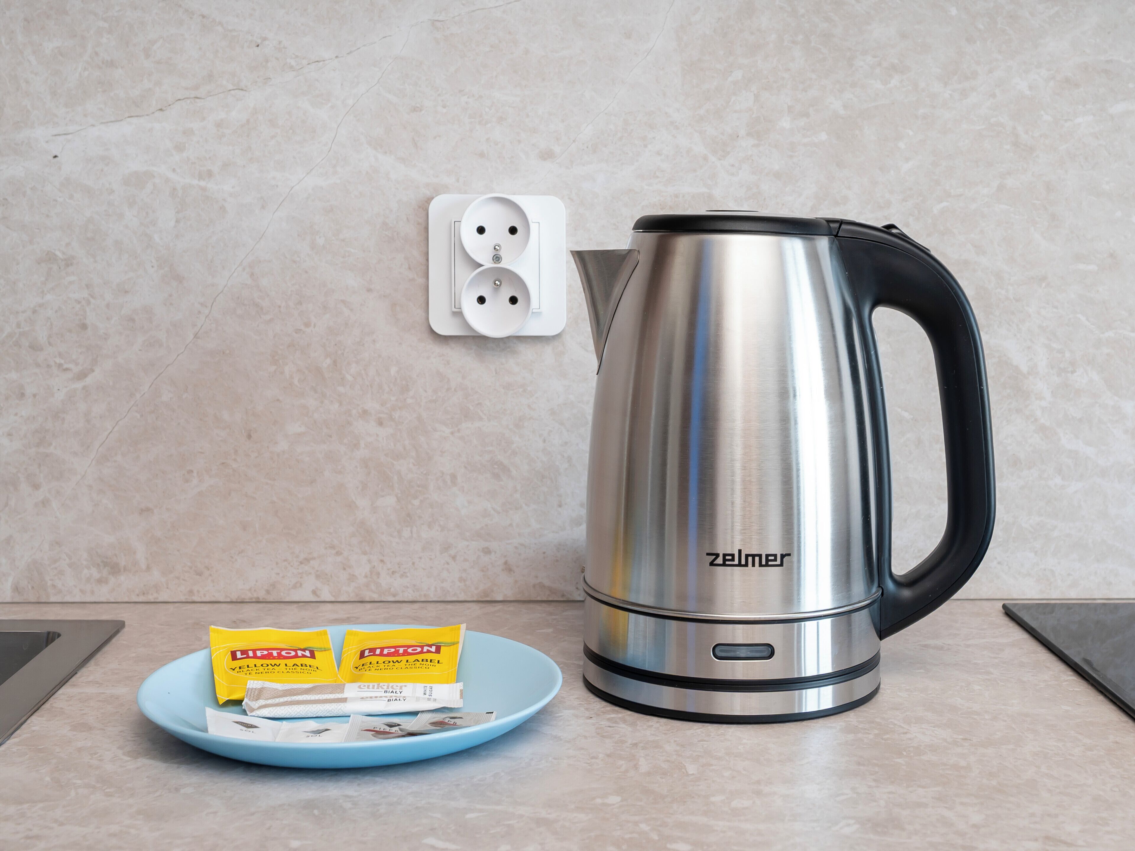 Una tetera sobre una encimera con una bandeja de bolsitas de té Lipton y un enchufe de fondo.