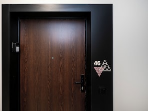 A wooden door with a digital lock and a keypad, and a wall with the number '46' and a geometric design.