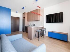 A modern kitchen with a built-in island, bar stools, and a flat-screen TV. - Łódź Fabryczna Modern Studio (Łódź)