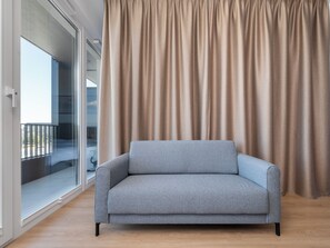 A grey sofa in a room with a large window and a curtain. - Łódź Fabryczna Modern Studio (Łódź)