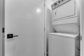 A white, modern laundry room with a door, a control panel with dials, and a shelf. - Modern 2BR Suite | Near YEG Airport & Amenities (Edmonton)