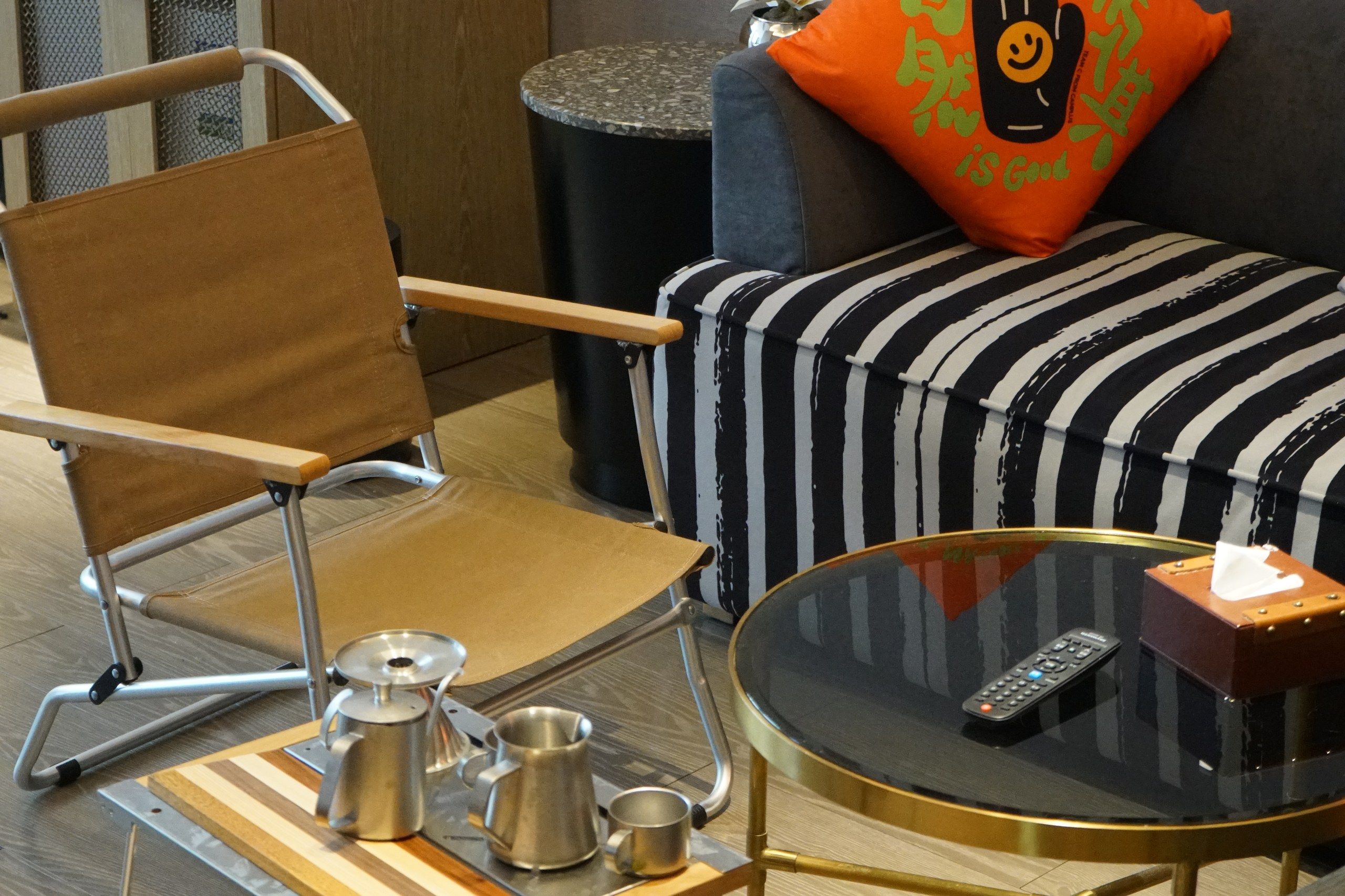 A modern living space with a foldable chair, a coffee table with a remote control, and a striped ottoman.