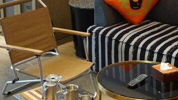 A modern living space with a foldable chair, a coffee table with a remote control, and a striped ottoman.