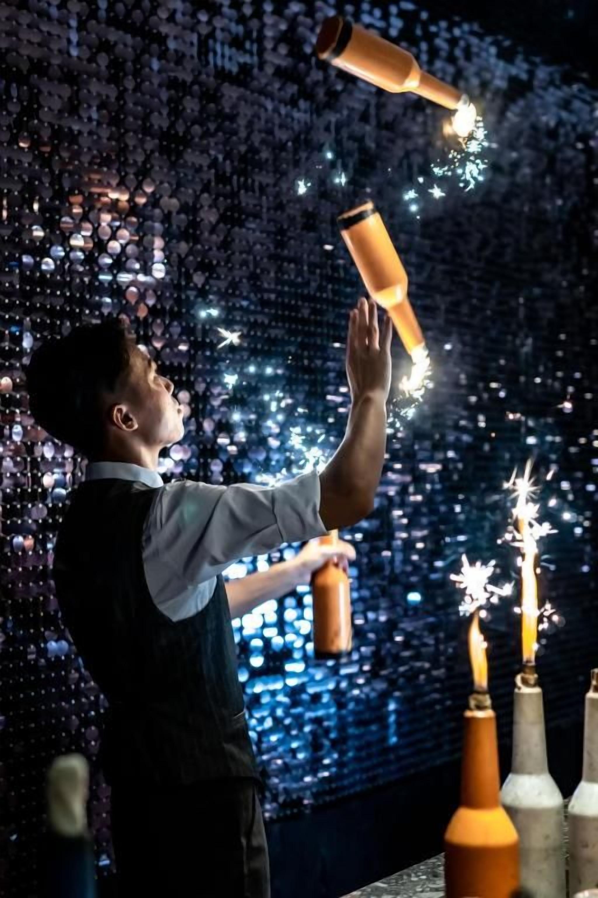 A person performing a bottle trick with bottles and sparks.
