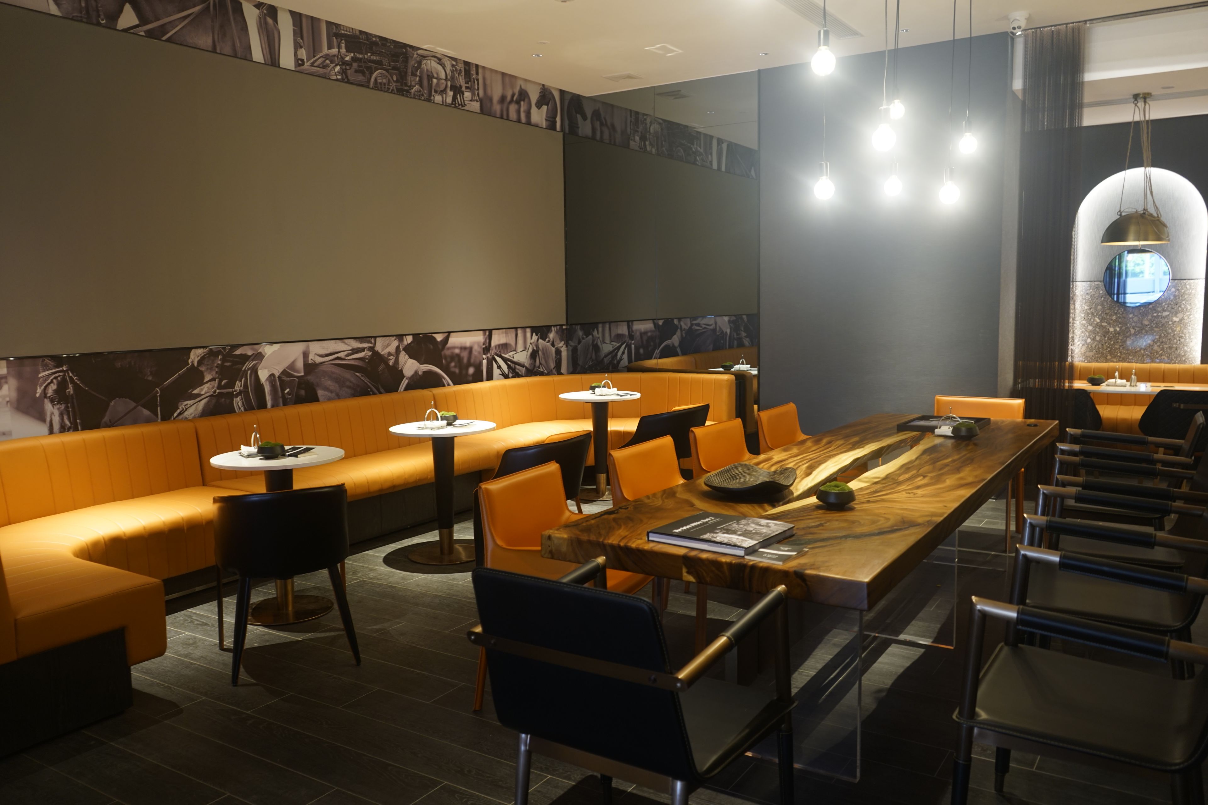 A modern restaurant with high tables, orange seating, and a large mural on the wall.