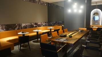 A modern restaurant with high tables, orange seating, and a large mural on the wall.