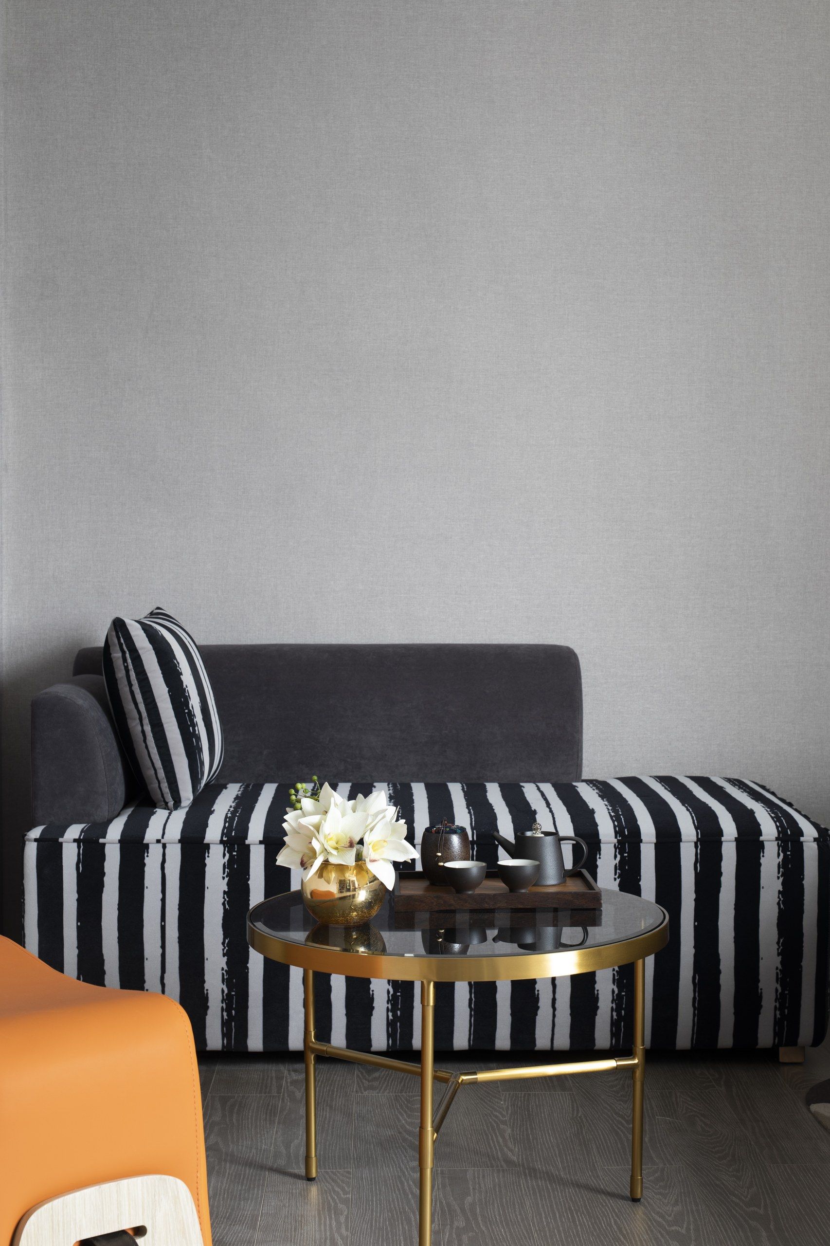 Una sala moderna con un sofá, una mesa de centro redonda de vidrio y un jarrón decorativo con flores.