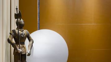 A statue of a knight holding a sword, a large white sphere, and a modern light fixture in a hallway with a yellow wall and white ceiling.
