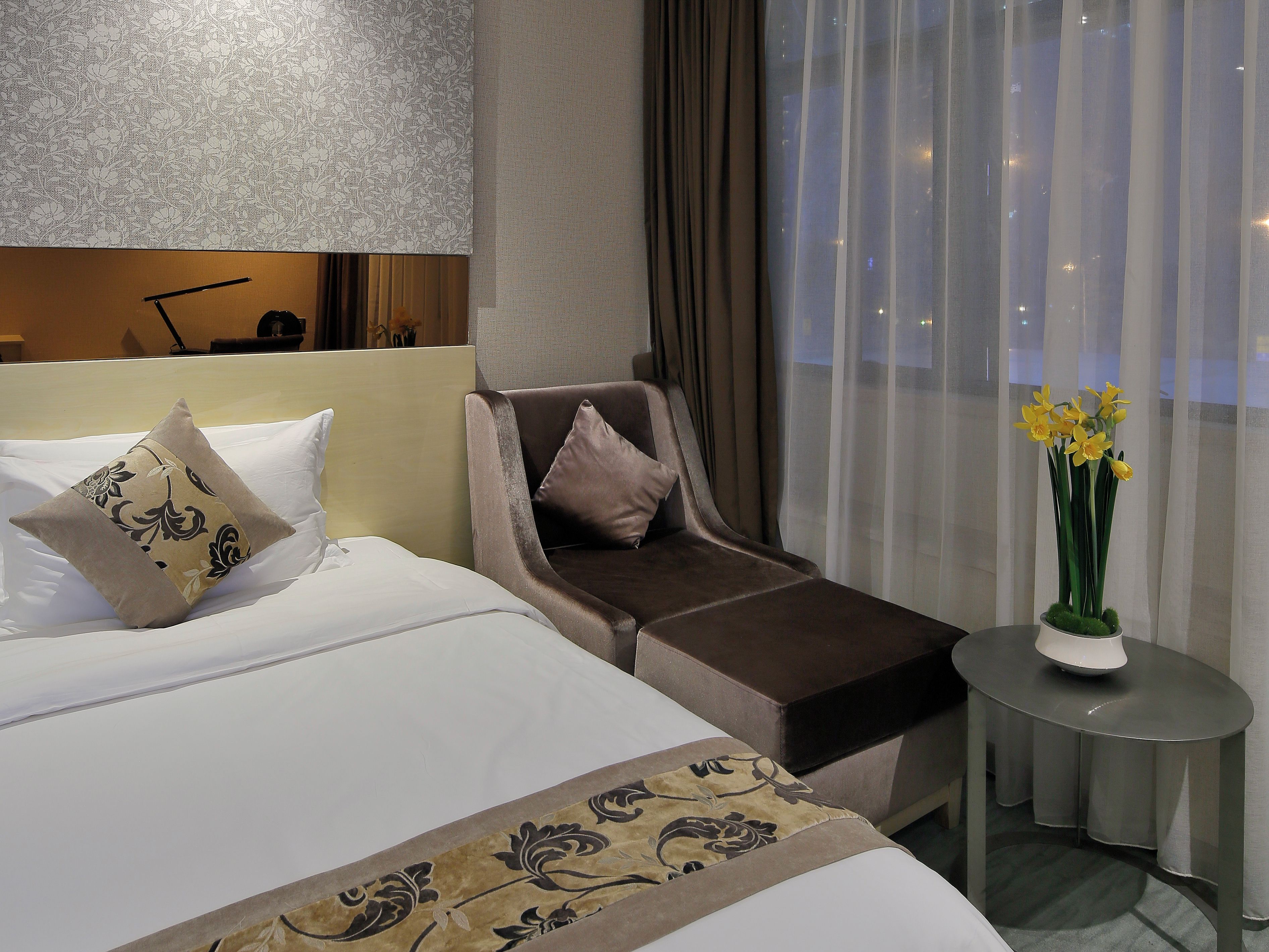 Habitación de hotel con cama, sofá, una mesita con un florero y vistas a través de cortinas translúcidas.