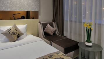Habitación de hotel con cama, sofá, una mesita con un florero y vistas a través de cortinas translúcidas.