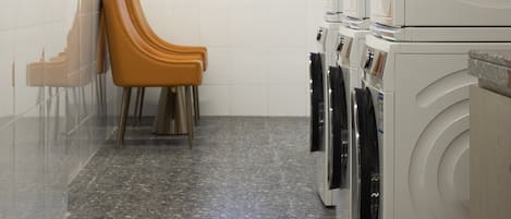 A laundry room with multiple washing machines, a seating area with chairs, and a large window providing a view.