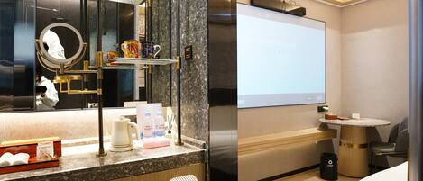 A hotel room with a large mirror, a coffee machine, a TV, and a small table with a chair.