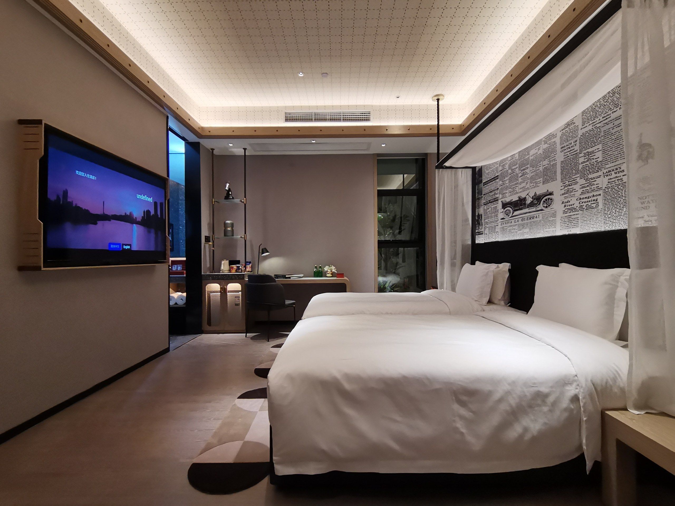 Una habitación de hotel moderna con una cama grande, un escritorio, un televisor y una pared con recortes de periódicos.