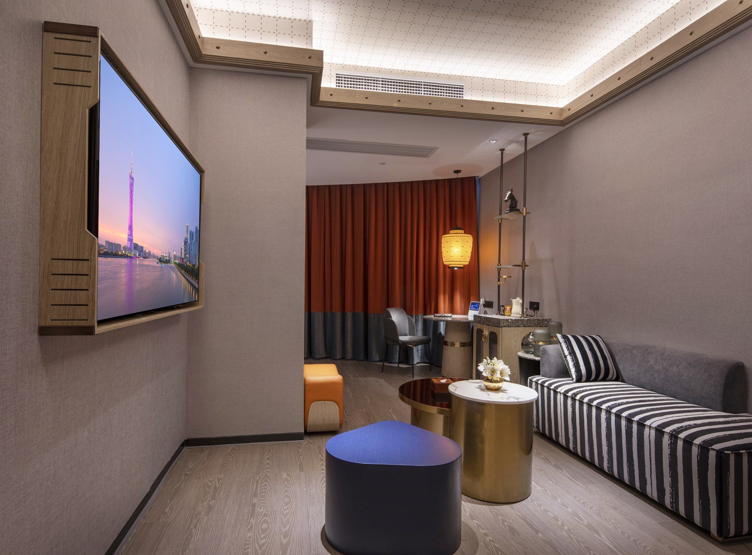 A hotel room with a large flat-screen TV mounted on the wall, a sofa, a coffee table, and a small round table with a lamp.