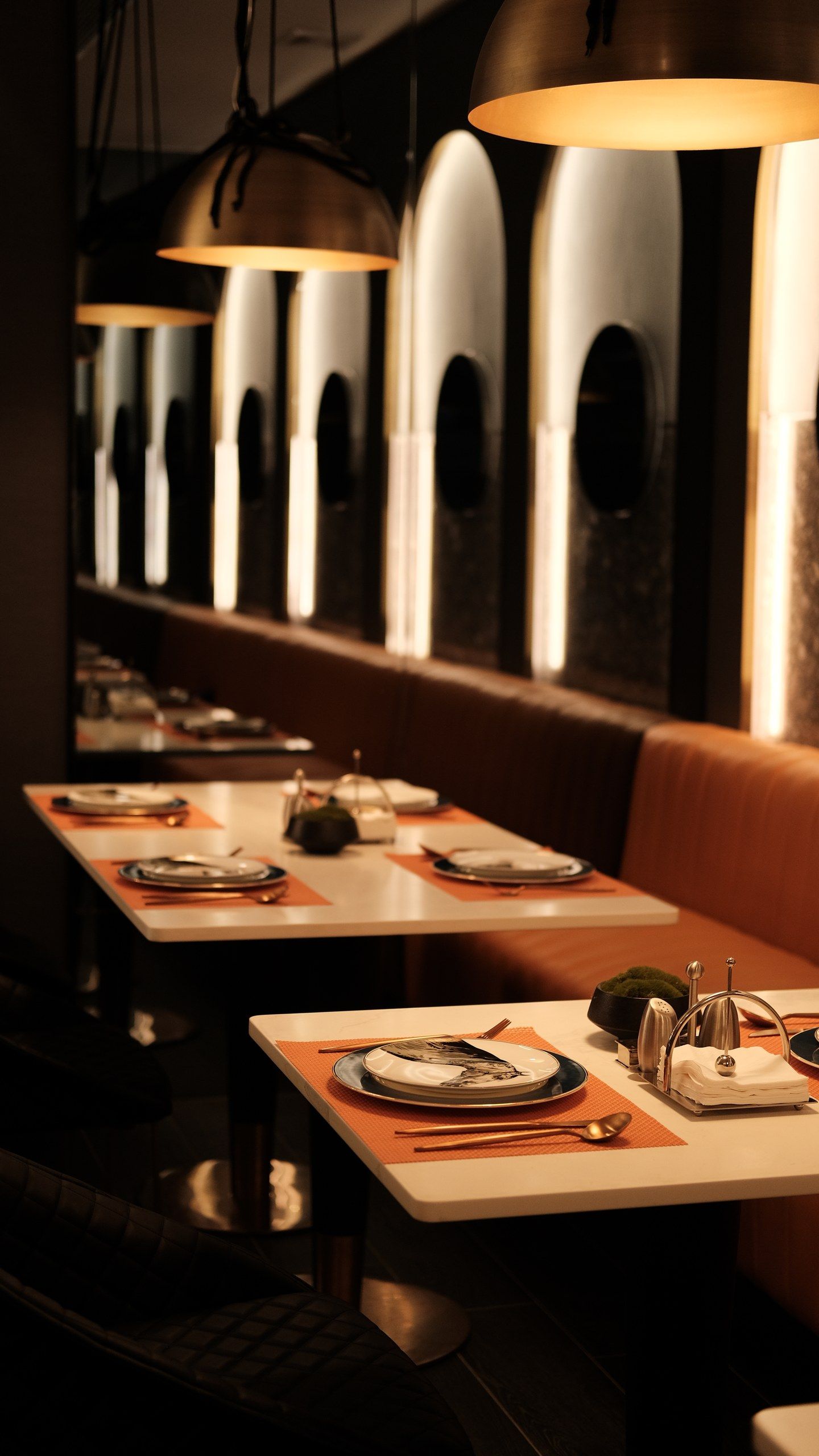 Interno di un ristorante con tavoli apparecchiati, illuminazione a sospensione e vista attraverso ampie finestre ad arco.