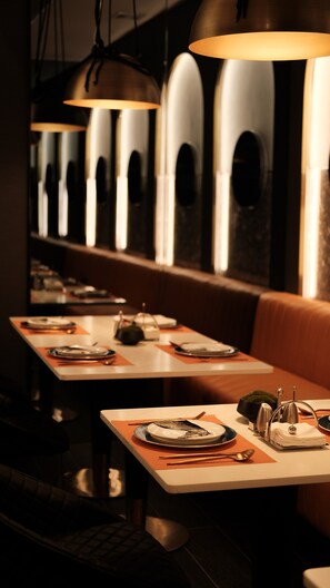 A restaurant interior with tables set for dining, overhead lighting, and a view through arched windows. - Arthur Hotel by Paco Zhujiang New Town (Guangzhou)