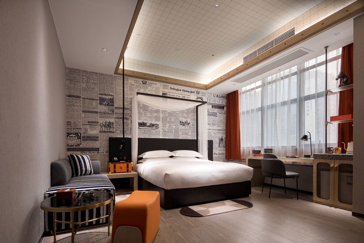 Quarto de hotel moderno com uma cama grande, uma escrivaninha, uma cadeira e um pequeno espaço de estar.
