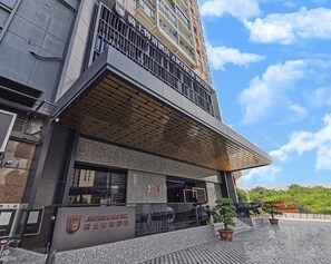 Un hotel con fachada moderna, una entrada destacada y cielo despejado al fondo.