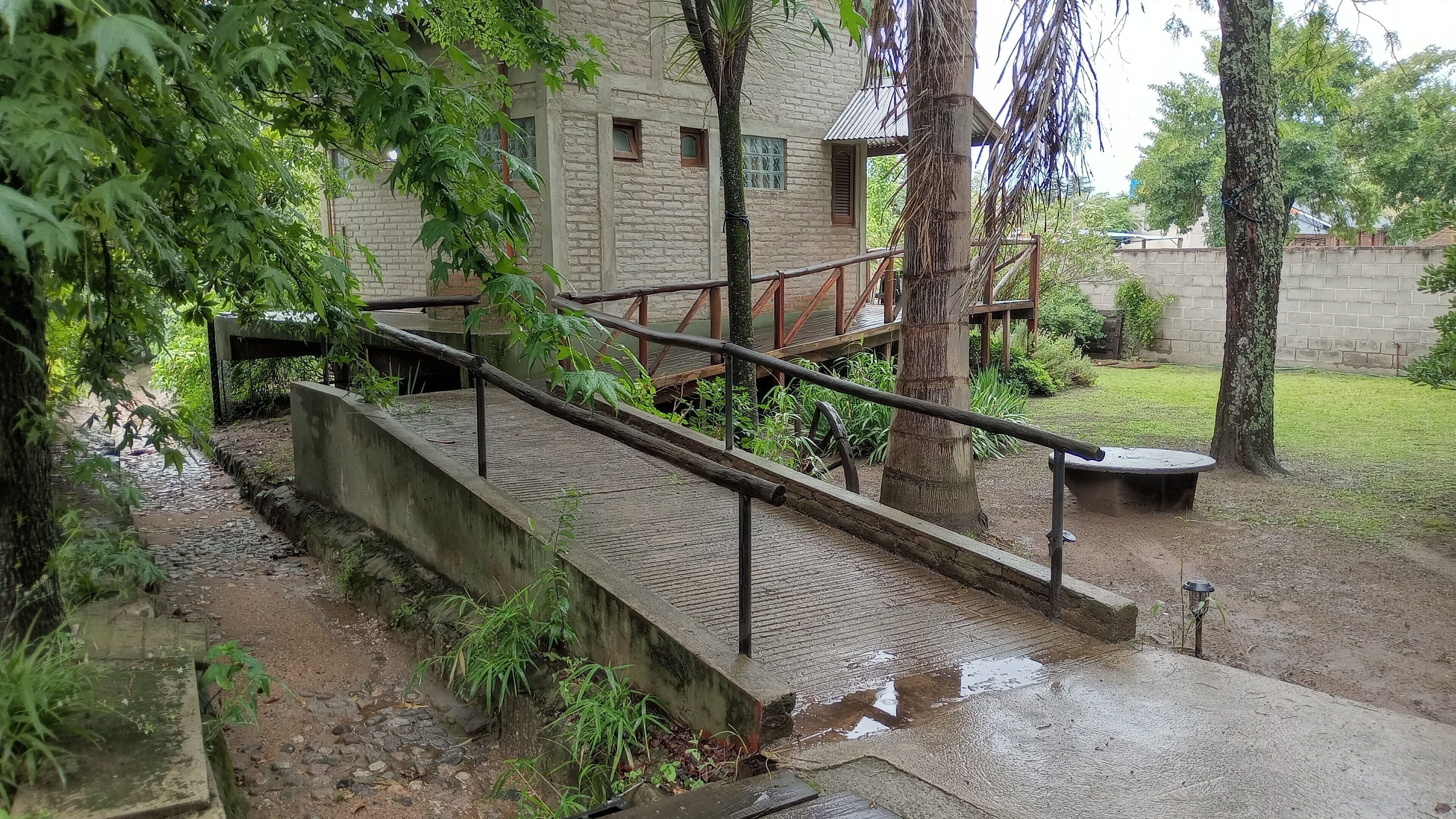 A concrete pathway leading to a building with a brick facade, surrounded by greenery and a small water feature.