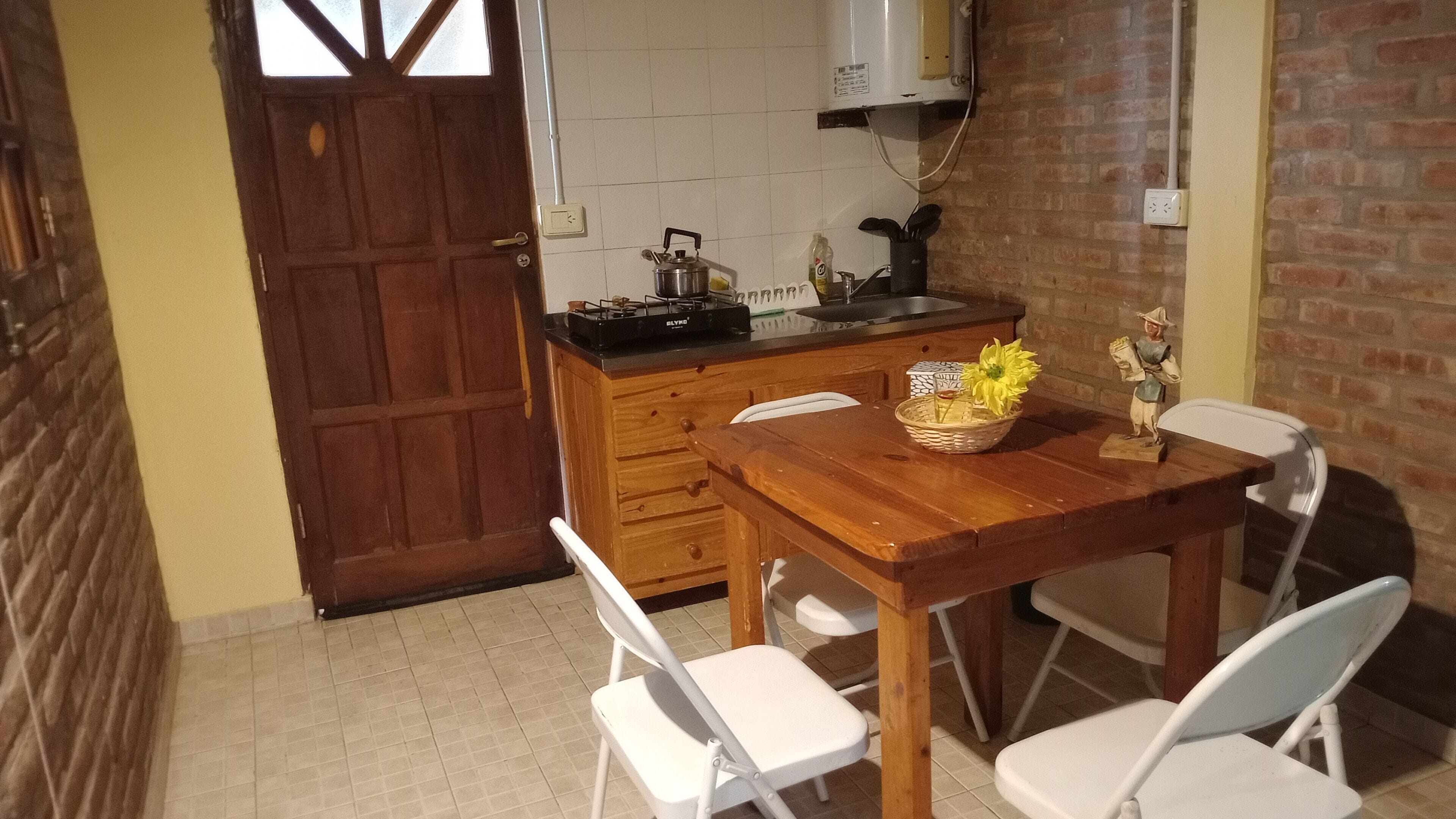 A kitchen with a wooden table, white chairs, a basket with a sunflower, and a gas stove.