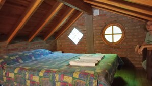 A room with a wooden ceiling, a brick wall, a window, and a bed with a quilt. - Cabañas Refugio LAS ACEQUIAS (Tanti)