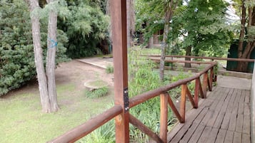 A wooden deck with a metal railing, surrounded by greenery and trees.
