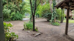 Un jardín con diversas plantas y árboles, un camino de grava y una zona delimitada por una cerca.