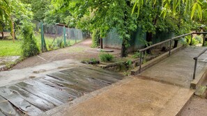 A wet wooden pathway leading to a green fenced area with a bench and a small garden.
