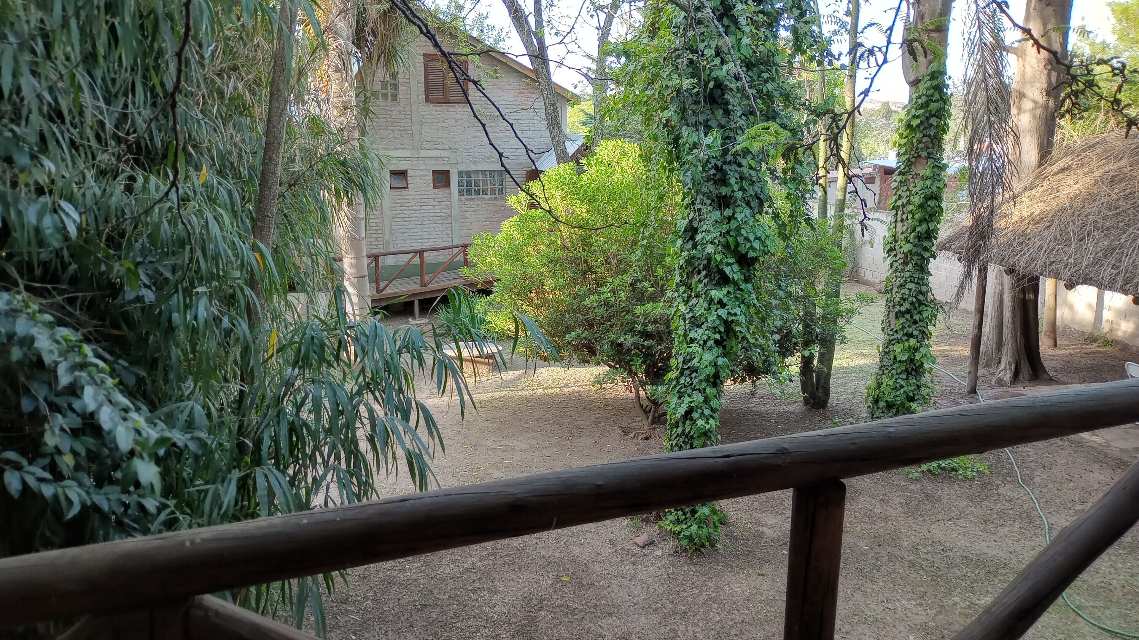 A rustic wooden fence, a stone building, and a variety of greenery.