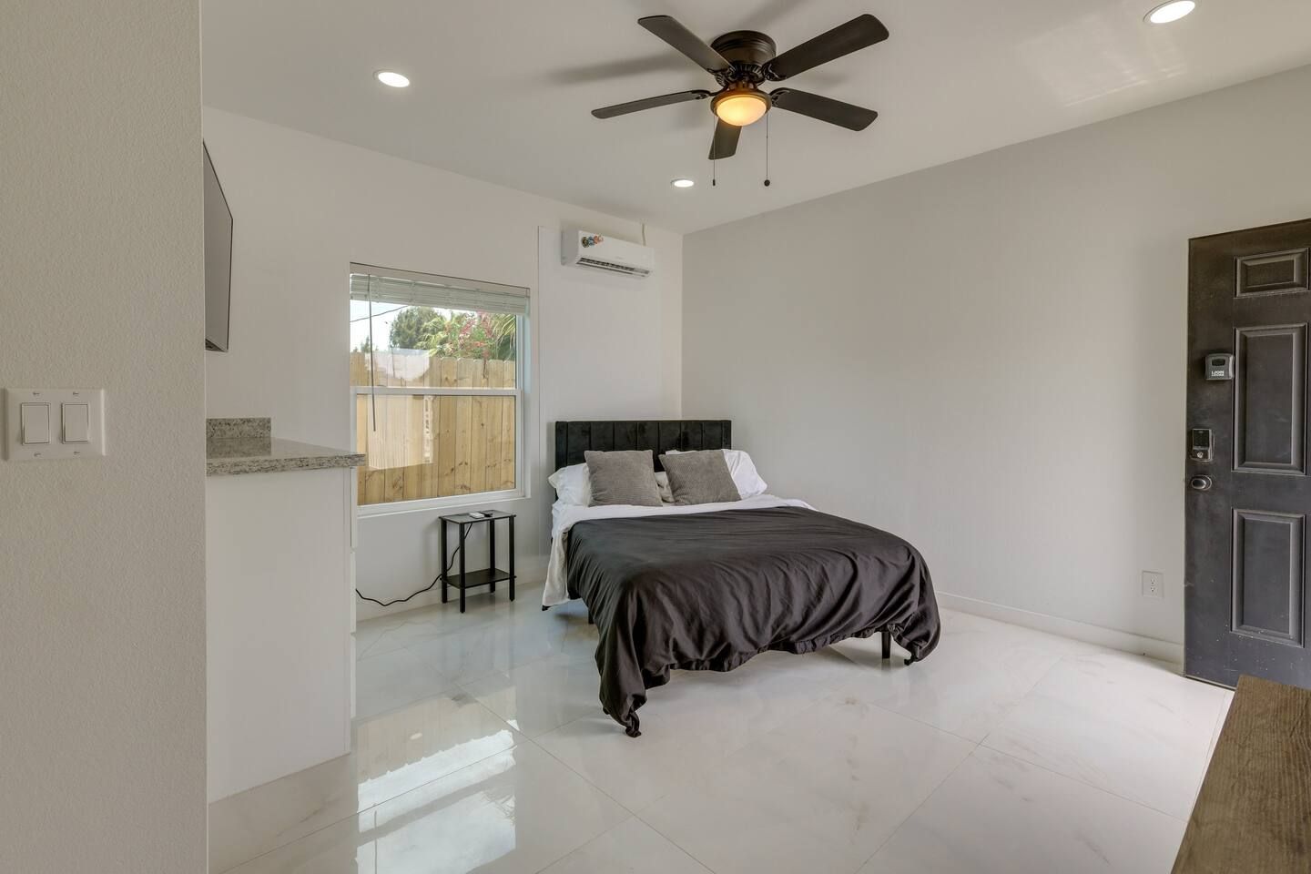 A bedroom with a bed, a desk, a chair, a ceiling fan, and a door.