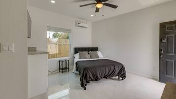 A bedroom with a bed, a desk, a chair, a ceiling fan, and a door.