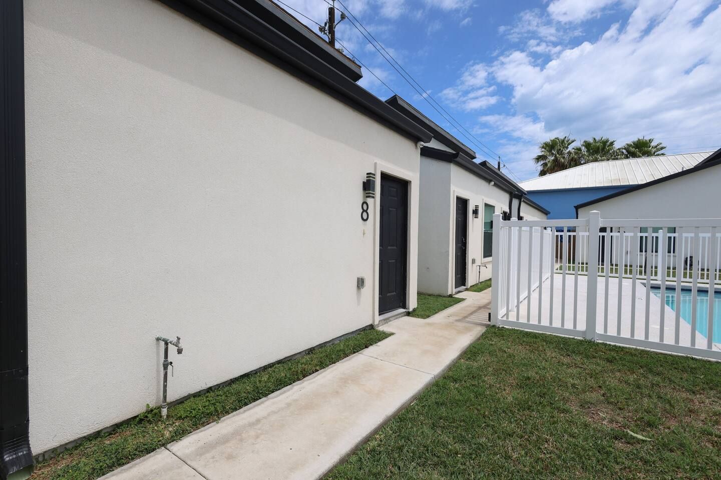 A residential property with a white exterior, a black door marked with the number 8, a concrete pathway, and a fenced swimming pool area.