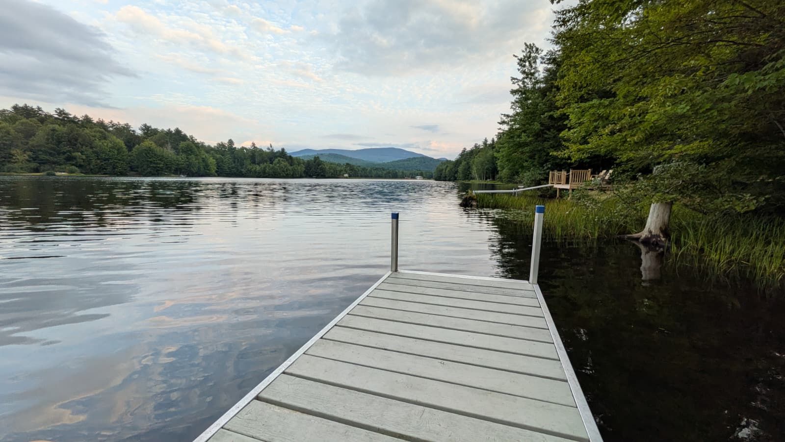 A wooden dock extending into a calm lake with a forested shoreline and distant hills.