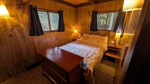 Quarto de cabana de madeira com cama, cômoda, abajures e cortinas.