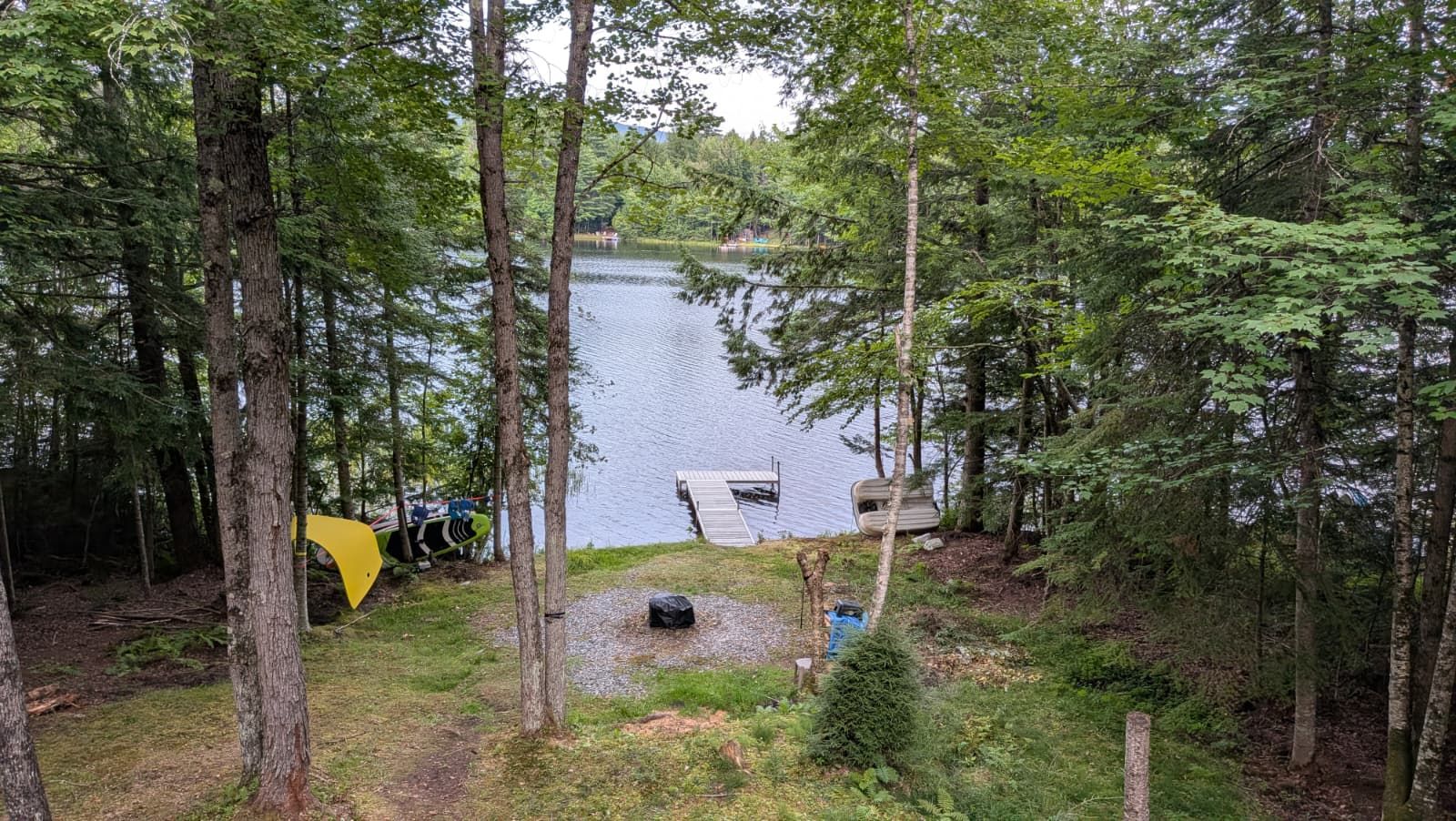 A forested area with a lake, a dock, and a yellow tent.