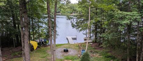 Une zone boisée avec un lac, un quai et une tente jaune.