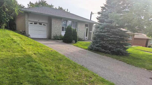 Une maison d’habitation avec un garage, une allée et une pelouse bien entretenue.