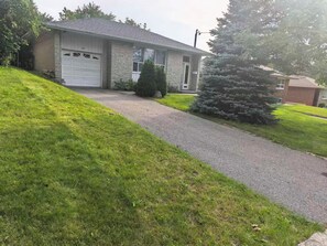 A residential house with a garage, a driveway, and a well-maintained lawn. - cozy three bedroom detached house with free parking (Toronto)