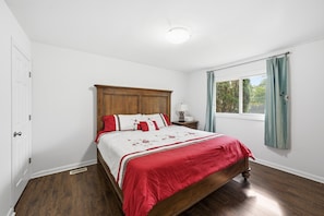 Un dormitorio con una cama de madera, paredes blancas, una ventana con cortinas y una puerta.