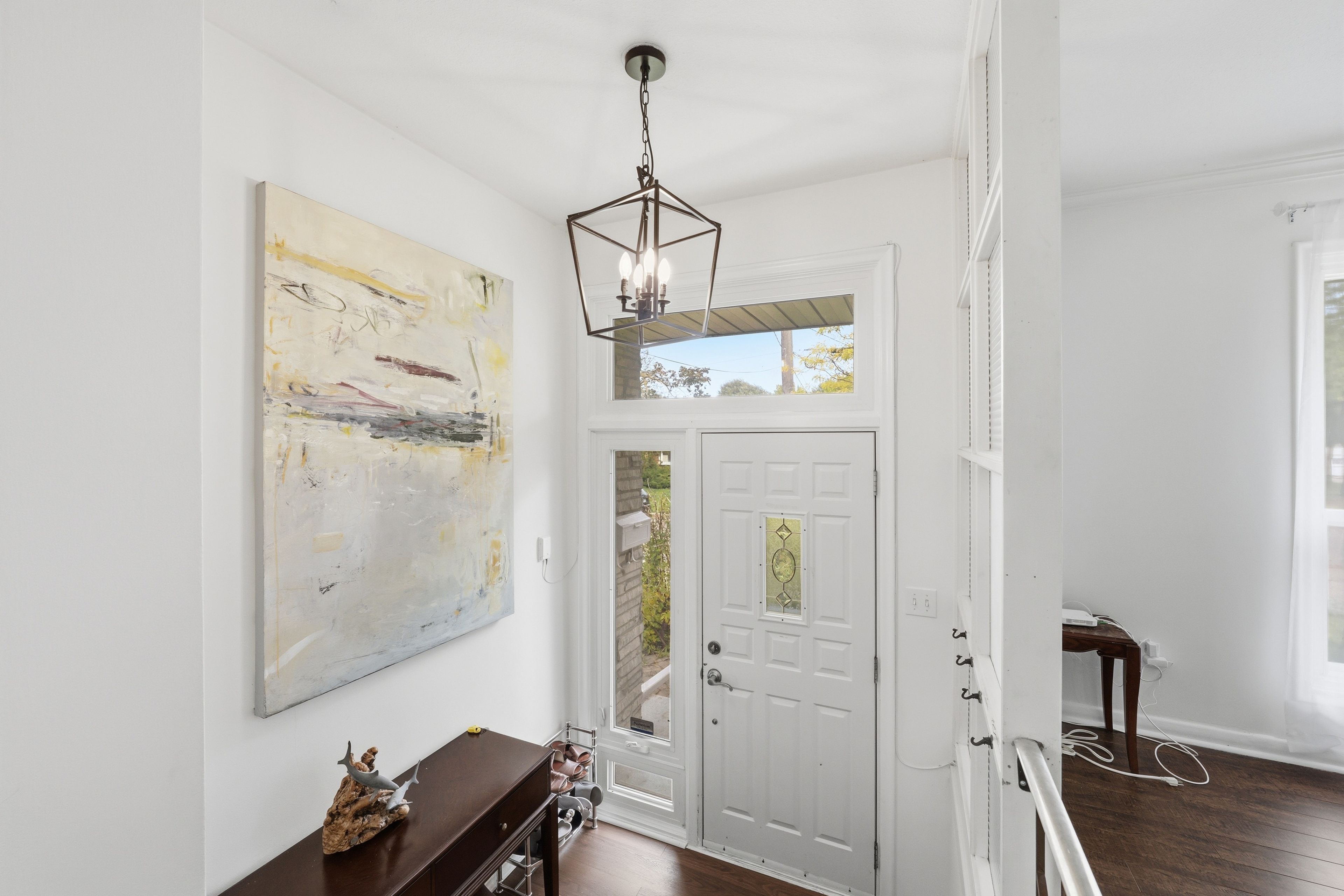 A hallway with a white door, a large abstract painting, and a wooden bench with shoes.