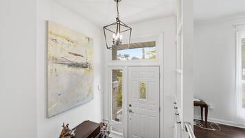 A hallway with a white door, a large abstract painting, and a wooden bench with shoes.
