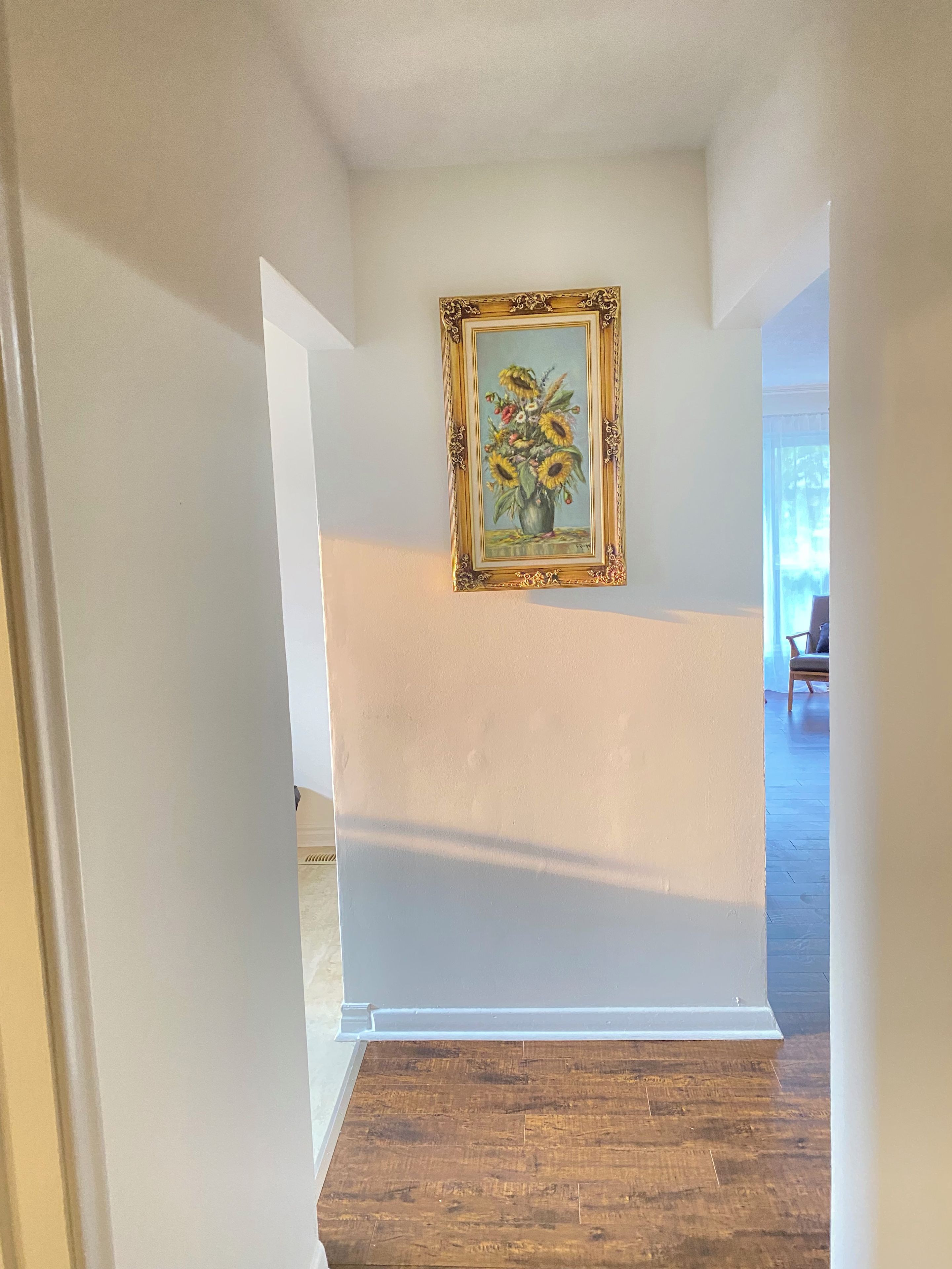 Un corridoio con pavimento in legno, pareti bianche e un quadro appeso raffigurante girasoli.
