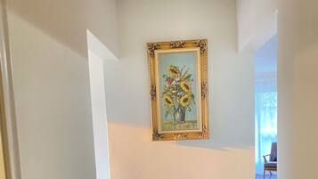 Un corridoio con pavimento in legno, pareti bianche e un quadro appeso raffigurante girasoli.
