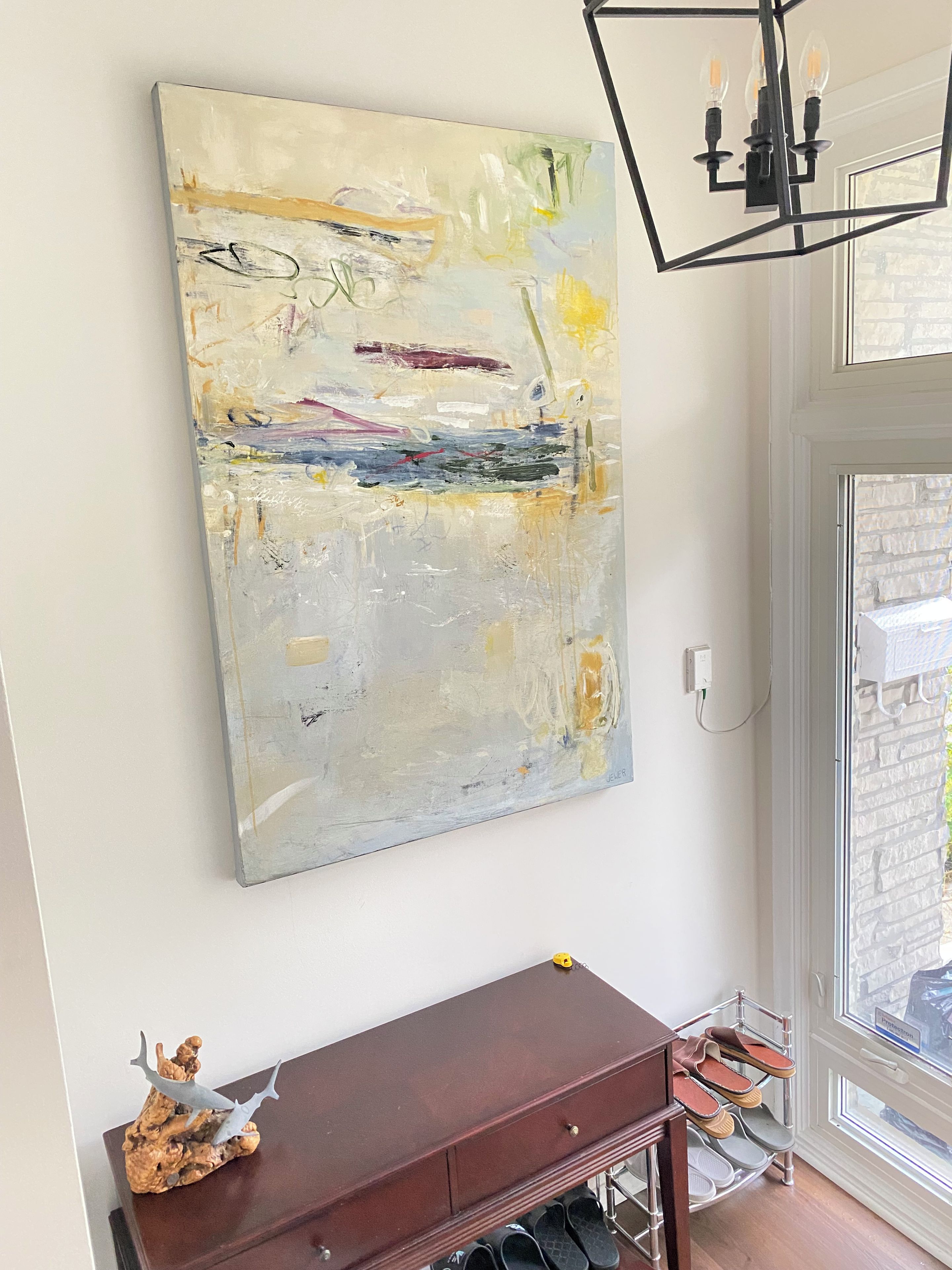 Una habitación con un cuadro abstracto grande en la pared, una consola de madera con zapatos y una araña.